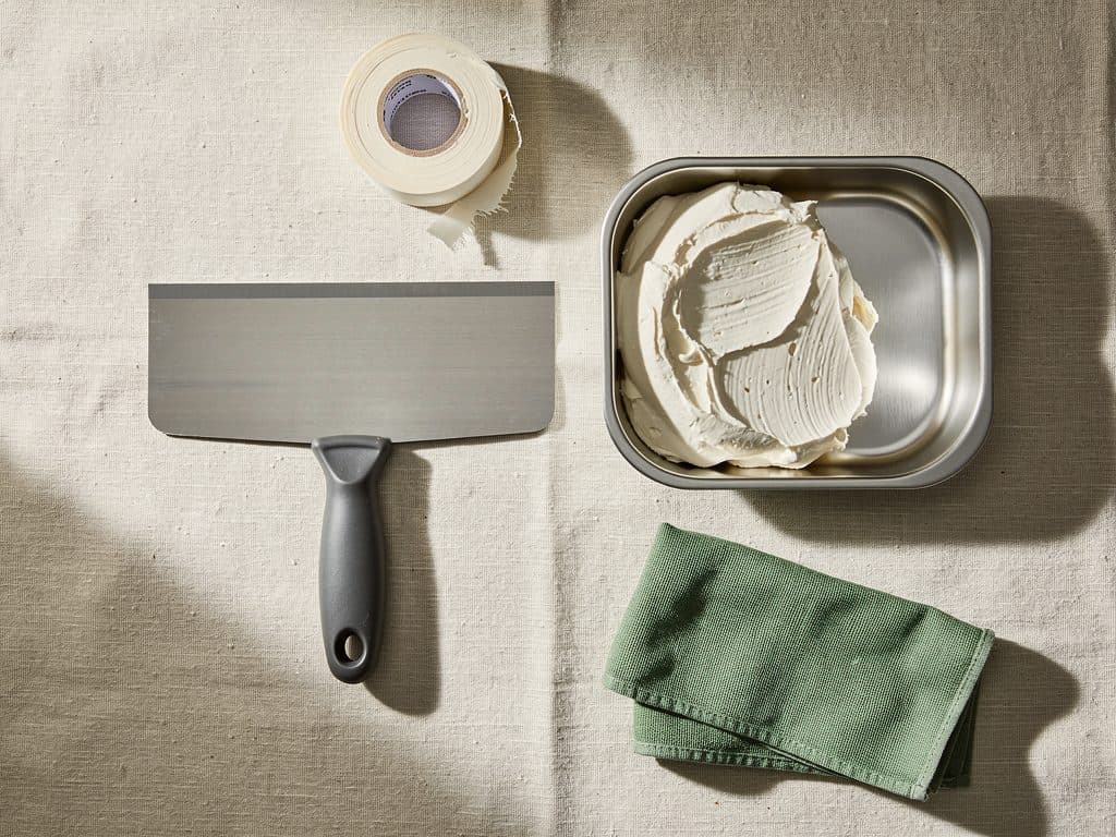 Taping knives, mud pan, and sanding block laid out on a drop cloth
