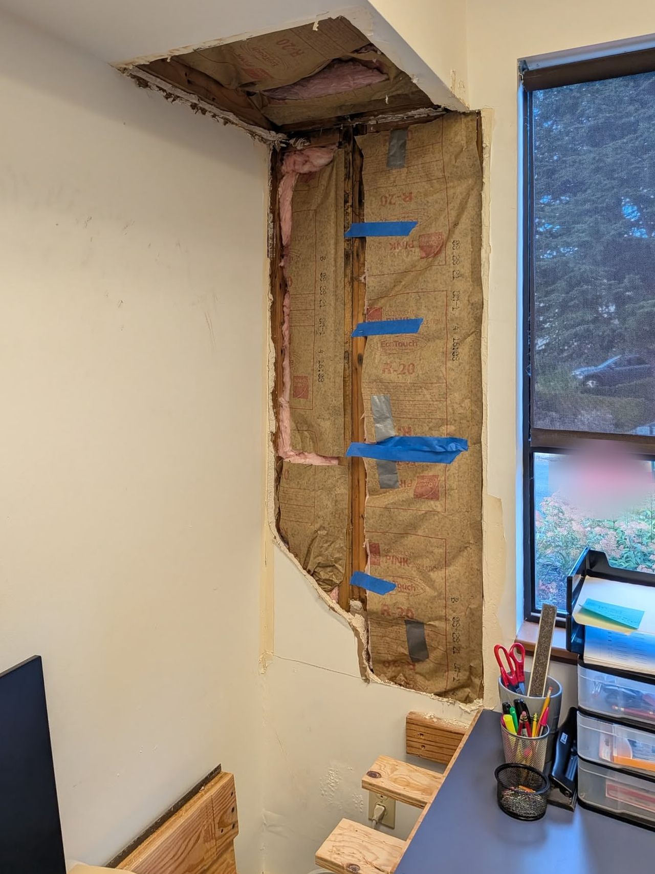 Wall and soffit beside an office window cut open to the studs and insulation