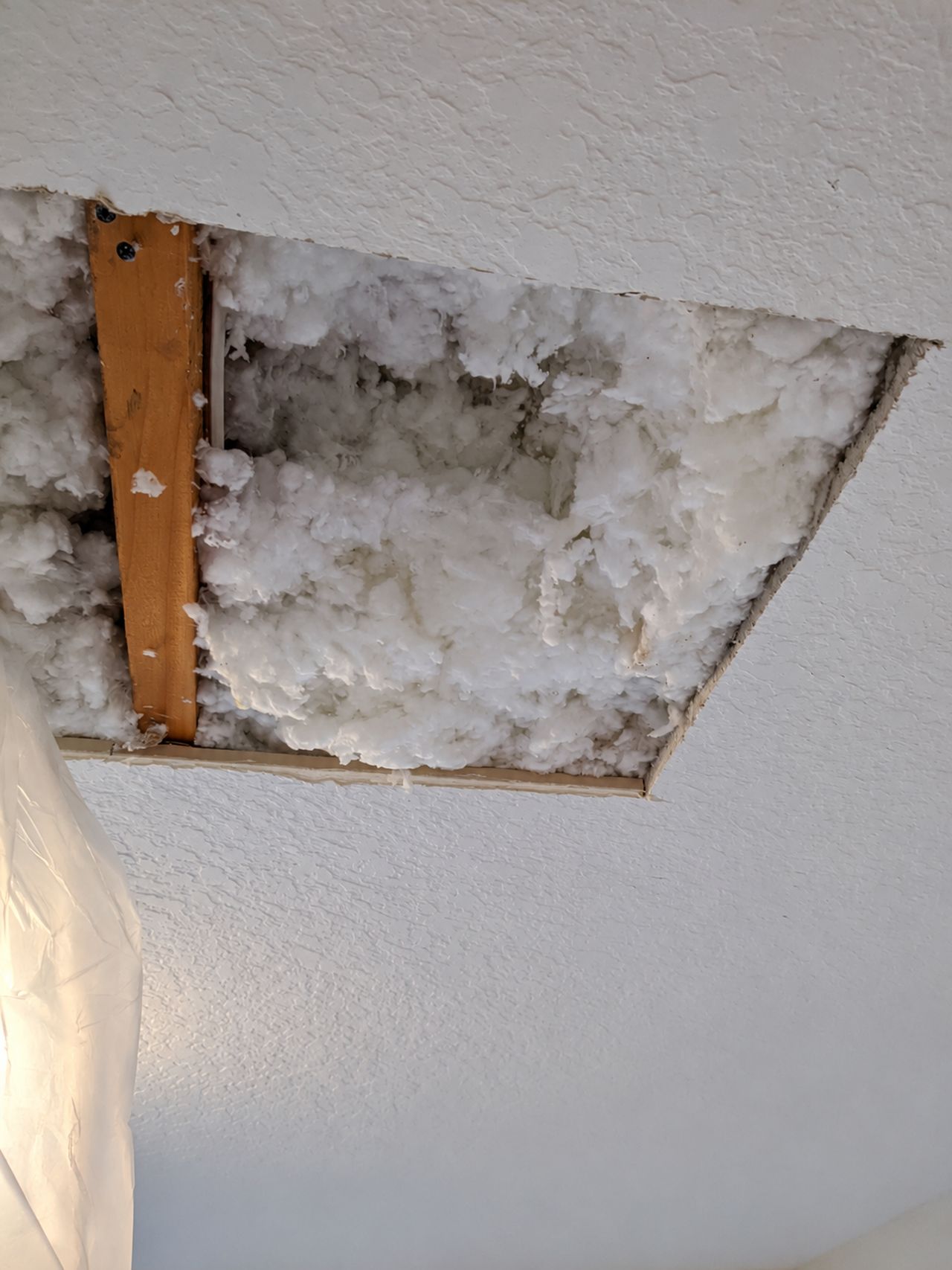 Hole in a textured ceiling with loose-fill insulation showing